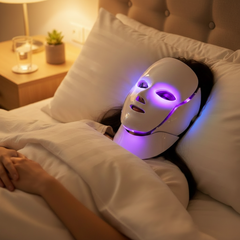 Woman wearing white LED light therapy face mask with purple light while relaxing in bed